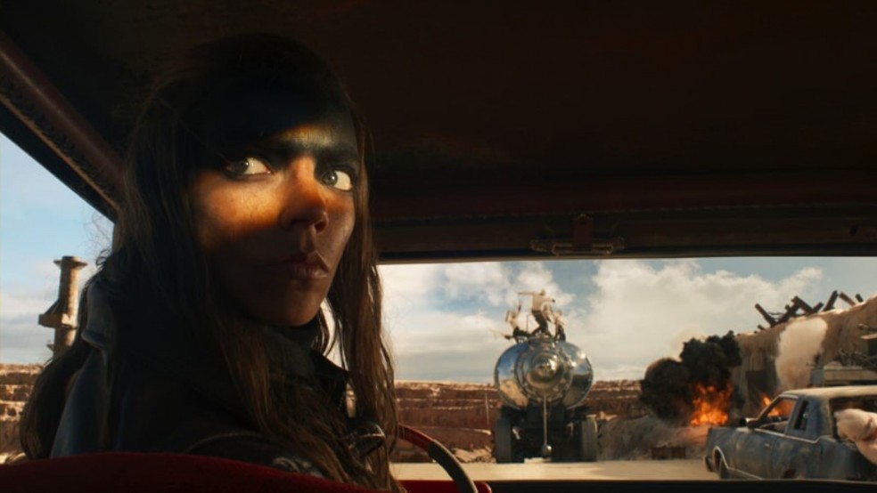 A woman with a painted forehead reverses a car in a desert