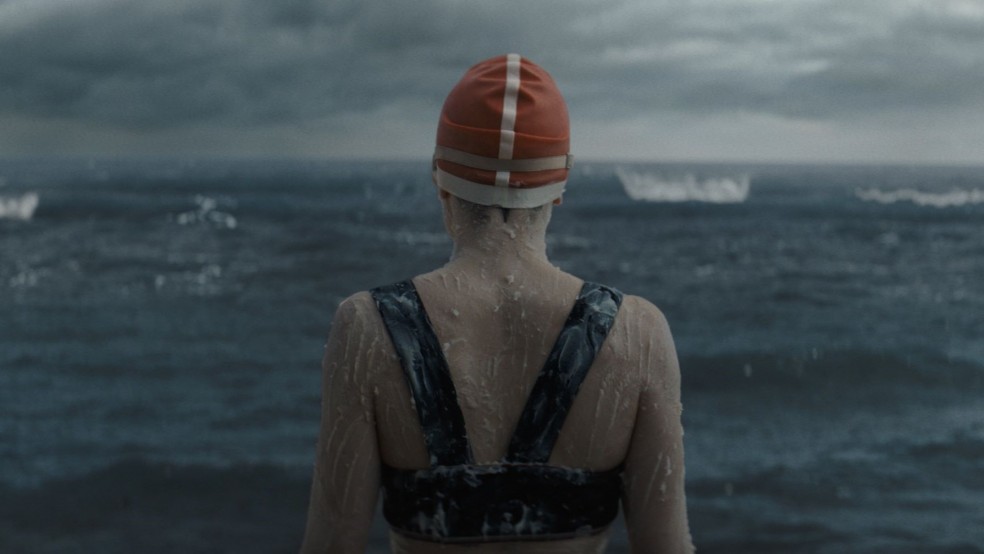 A woman wearing a bathing suit and swimming cap looks at the sea.