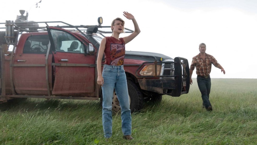A man and a woman stand in front of a truck in heavy wind