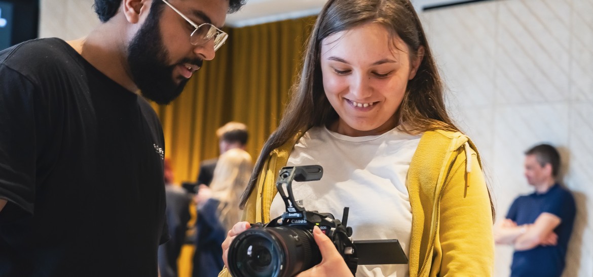 Young person using a camera with instructor helping