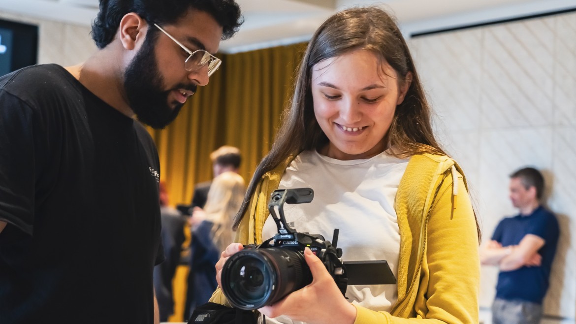 Young person using a camera with instructor helping