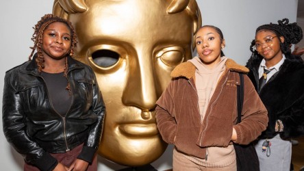 Three girls pose with BAFTA statuette.