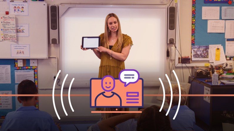 A teacher standing in front of her class holding a tablet device.