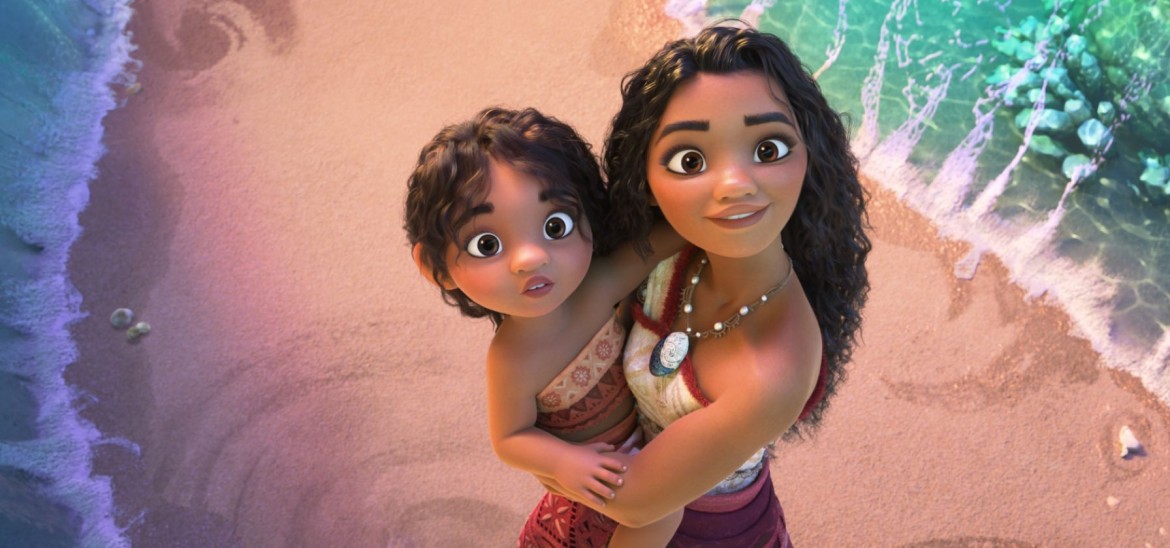 A young woman holds a child on a beach as they look up in aww.