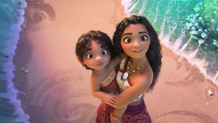 A young woman holds a child on a beach as they look up in aww.