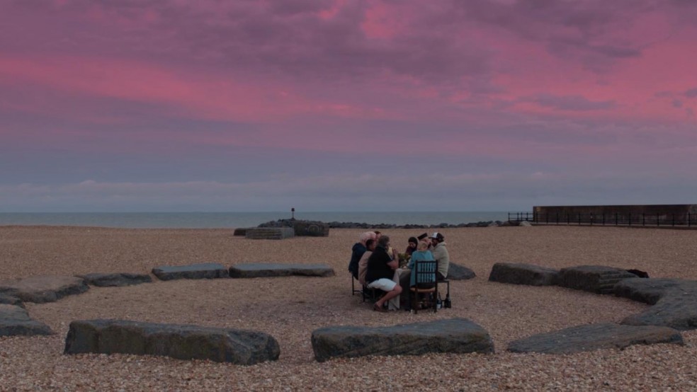 A beach at dusk on which there is a small group of people having dinner.