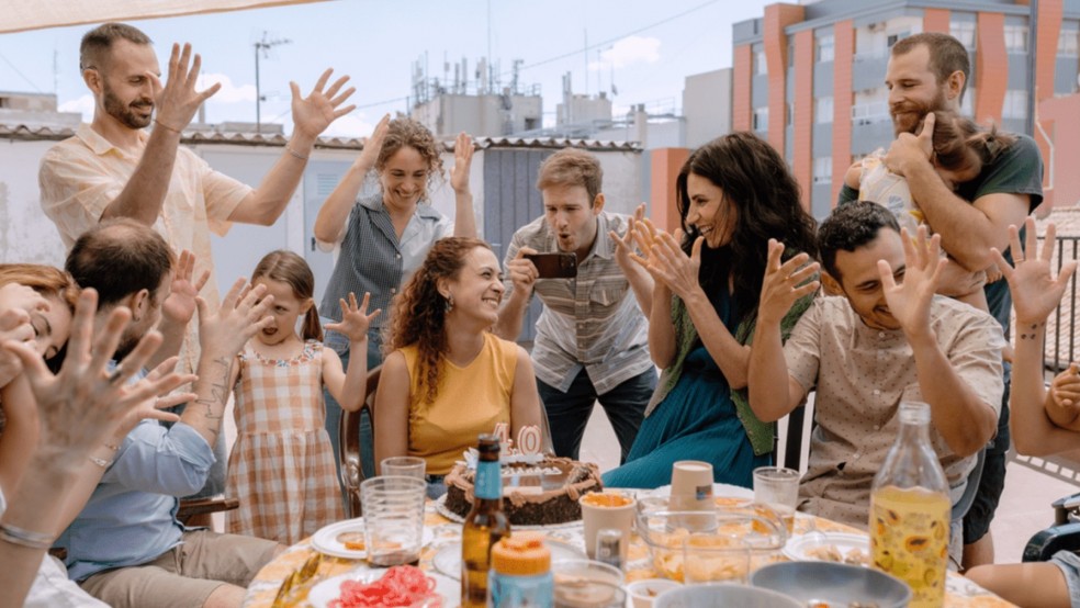 A group of people wave their hands in celebration on a rooftop terrace.