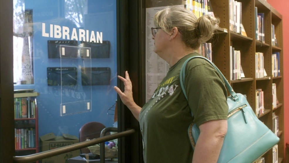 A woman next to a bookcase pushes a glass door with the sign 'Librarian'
