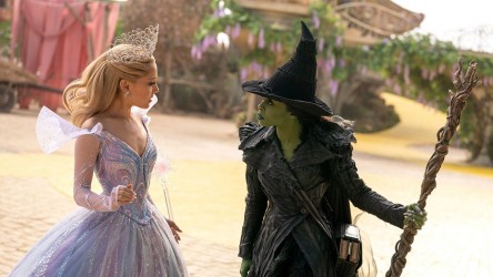 A blonde woman in a pink dress faces a green woman in a black witch outfit.