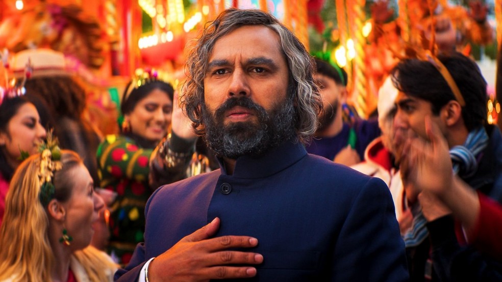 A bearded man stands pensively in the midst of a crowd at a Christmas fair.