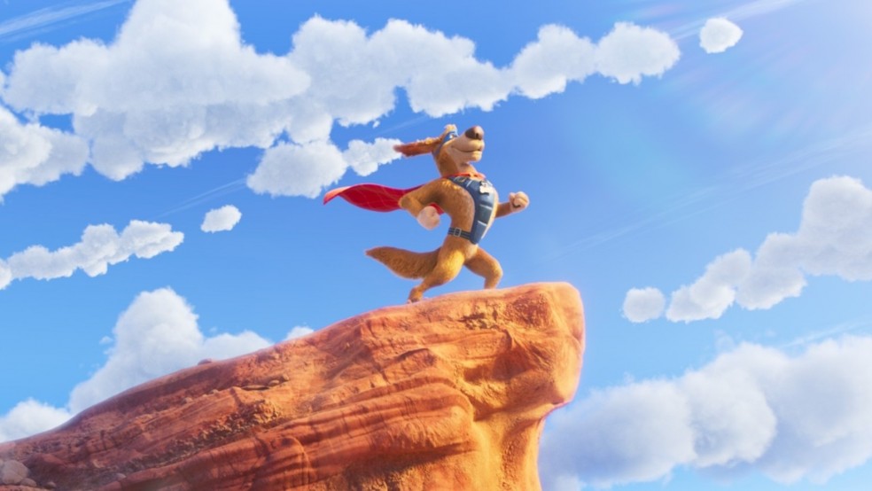 A dog stands on its hind legs wearing a superhero outfit on a cliff.