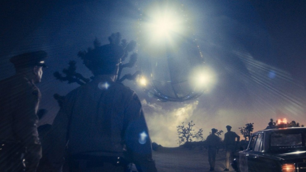 Several police officers stare at a large glowing UFO in the night's sky.