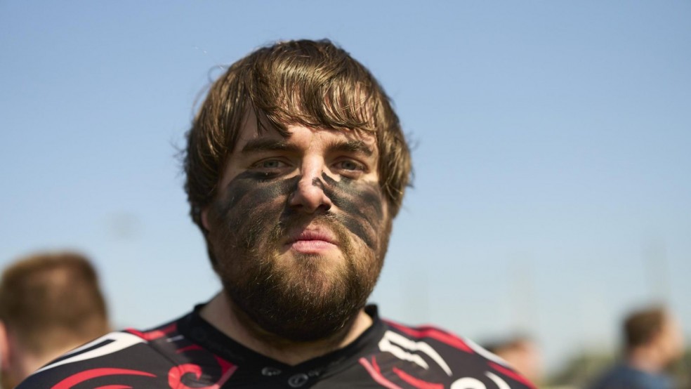 A man wearing a rugby top with mud markings on his face.