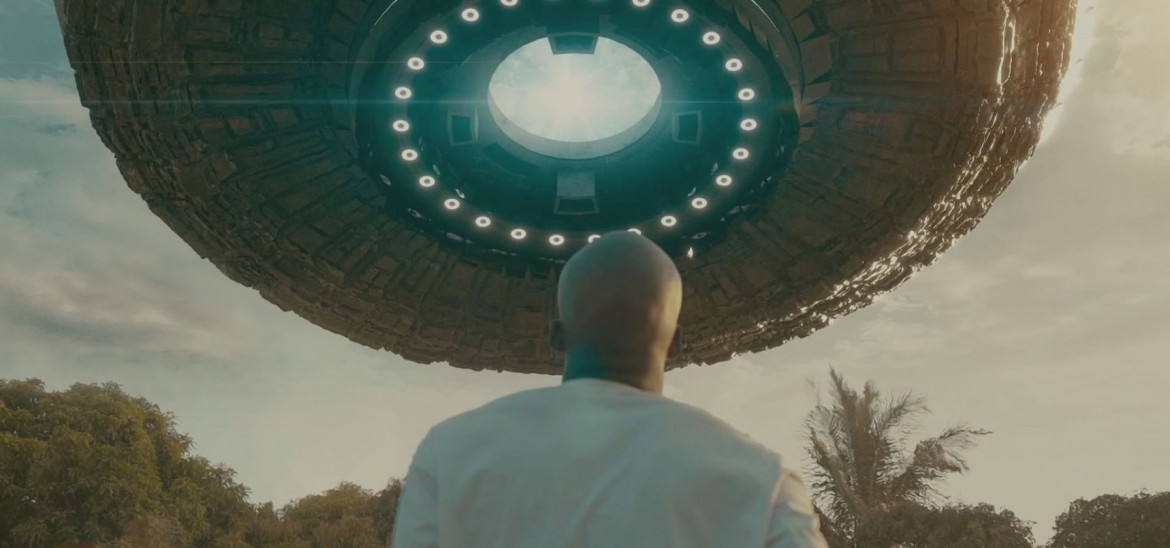 A man looks up at a space ship at dusk in an outdoor space.