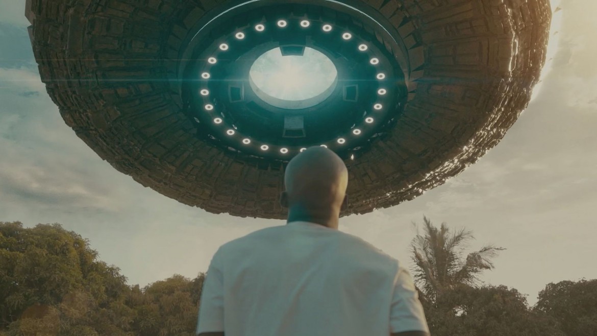 A man looks up at a space ship at dusk in an outdoor space.