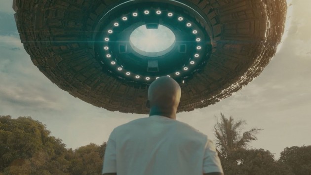 A man looks up at a space ship at dusk in an outdoor space.
