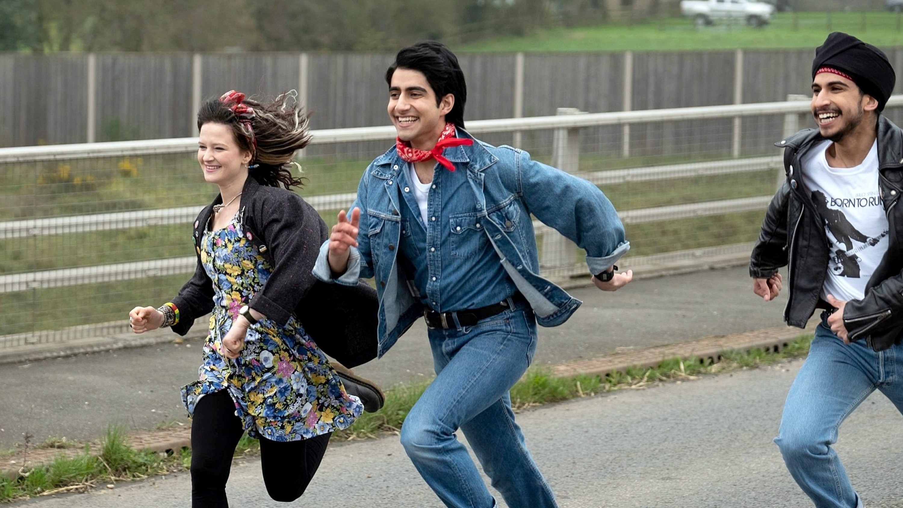 Three young people run happily through a street.