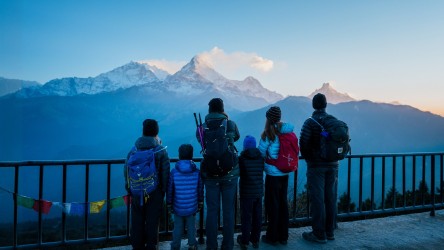 A family group in hiking gear stand by a railing looking at a mountain.