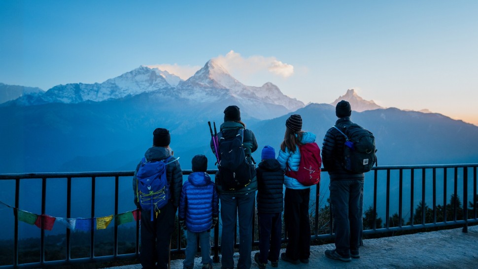 A family group in hiking gear stand by a railing looking at a mountain.